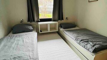 Ein kleines, kompaktes Zimmer mit zwei Einzelbetten, einem Fenster mit Vorhängen und einer kleinen Regalwand.