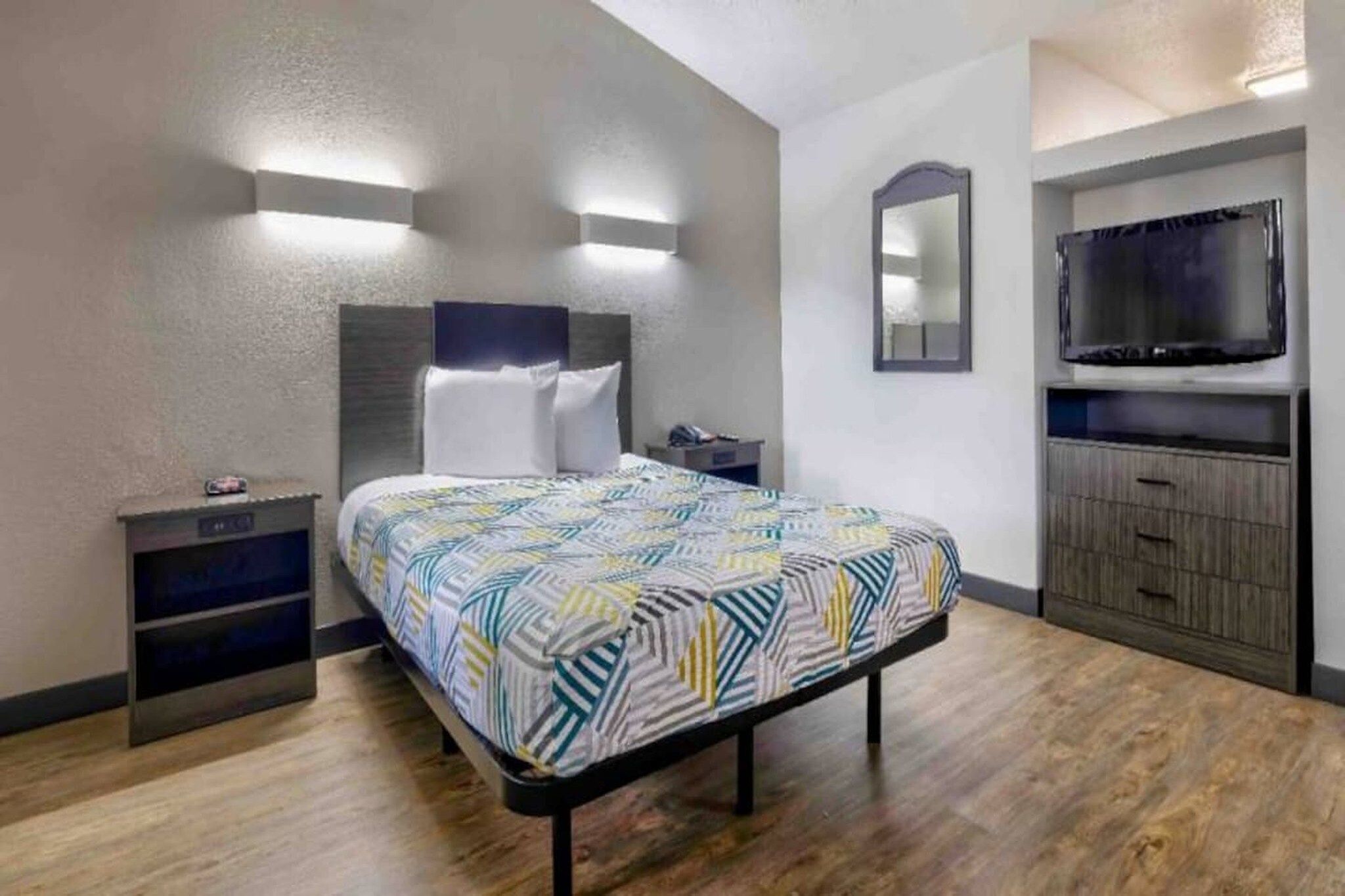 A hotel room with a bed, bedside tables, a TV, a mirror, and a wardrobe.