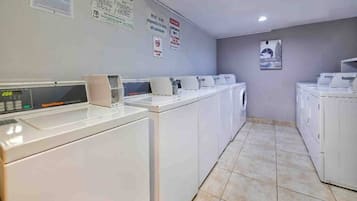 A laundry facility with multiple washing machines and dryers, a digital control panel, and informational posters on the walls.