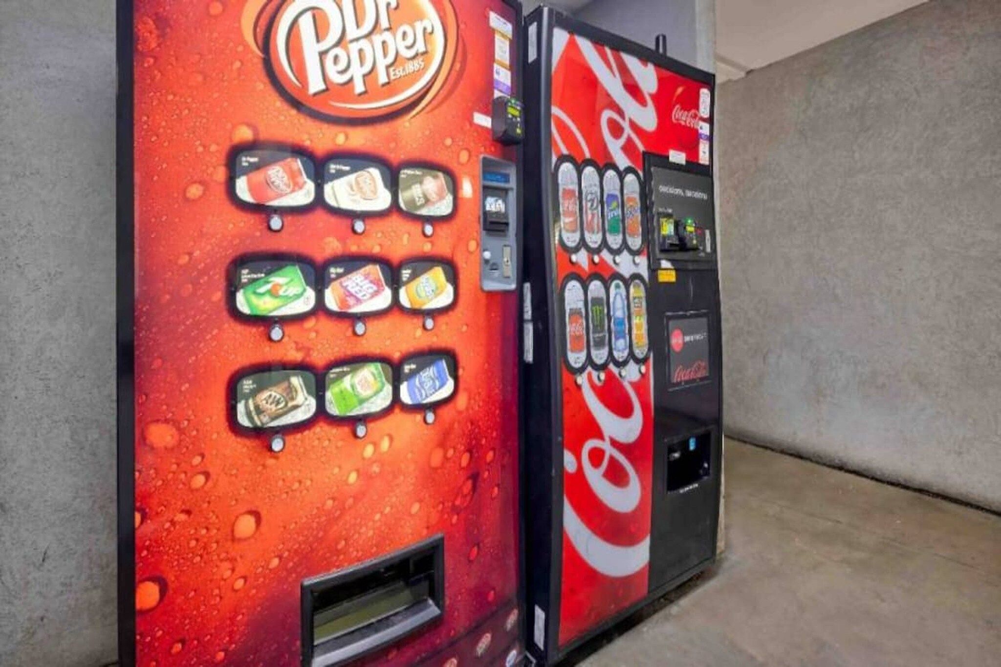 Two beverage vending machines, one for Dr Pepper and one for Coca-Cola, with various drink options.