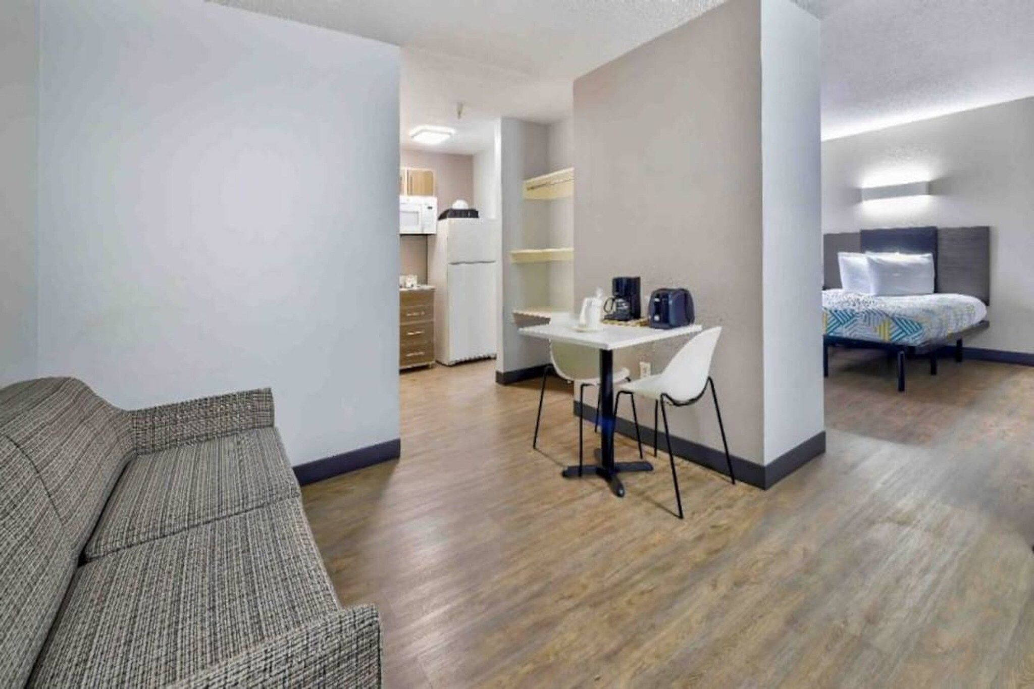 Ett modernt hotellrum med en soffa, ett matbord med stolar, en liten köksdel och en säng med sänggavel.