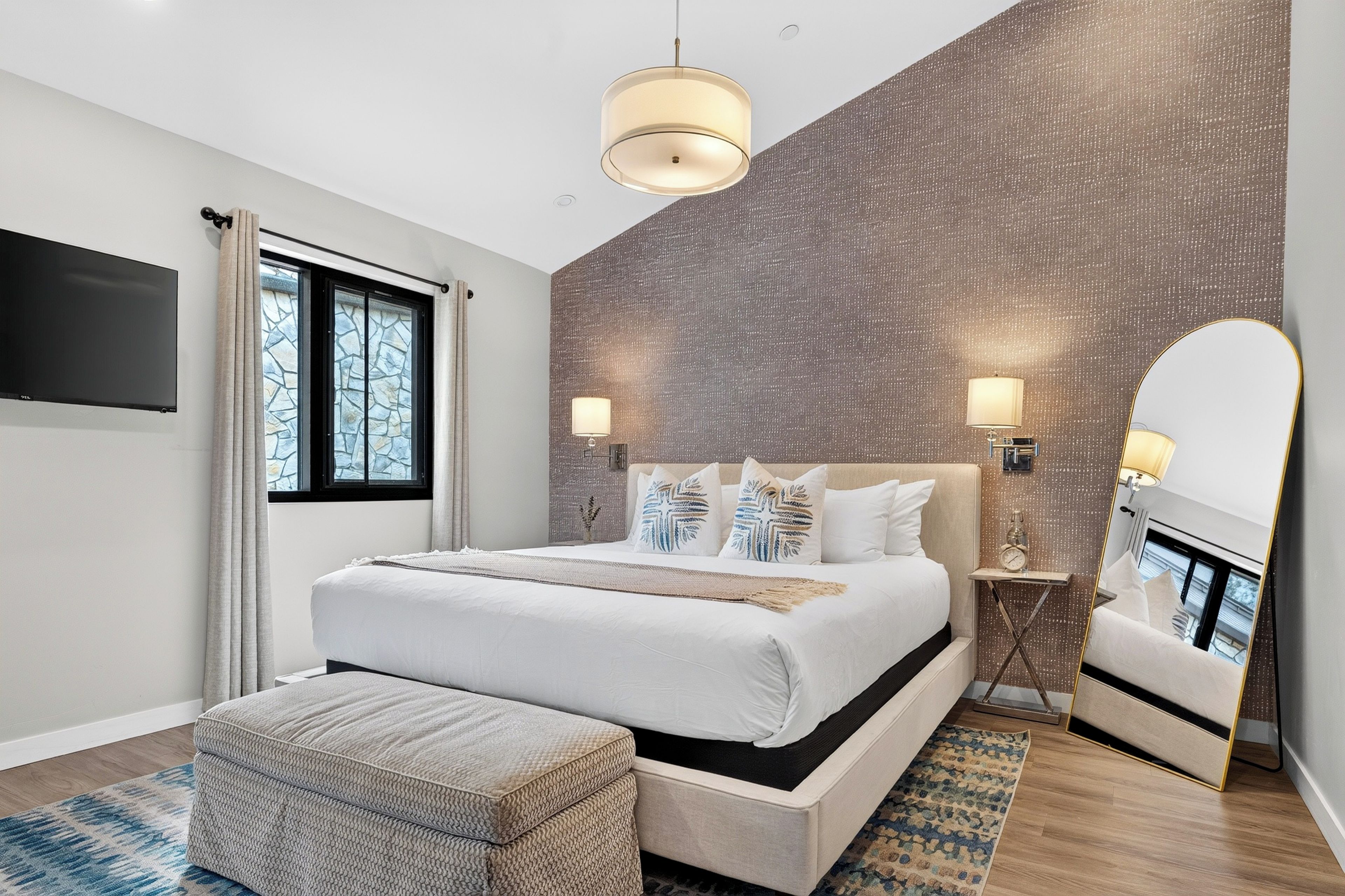 Rest easy in the studio's king bed, framed by a textured accent wall, warm lighting, and a full-length mirror.