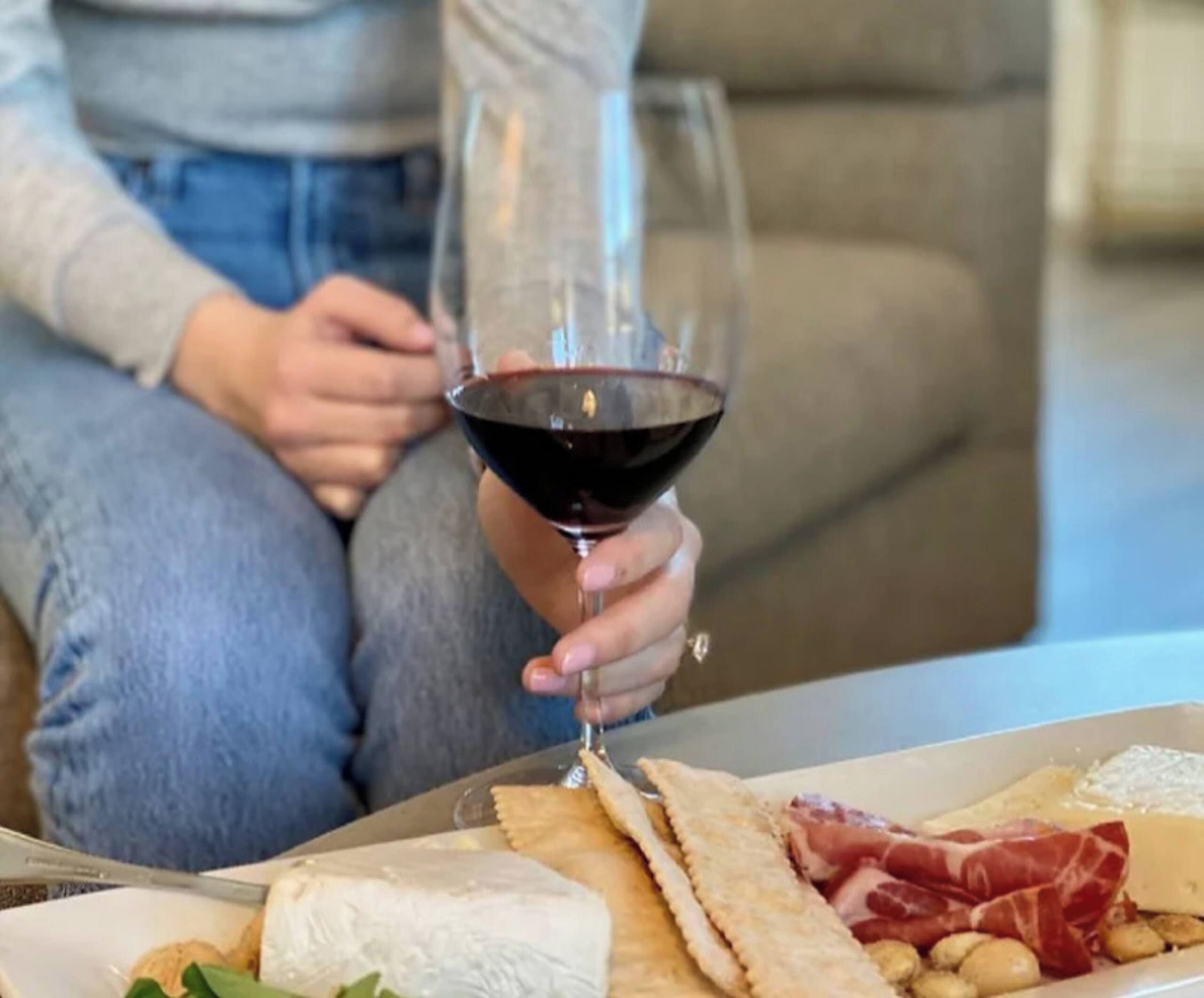 Una persona sosteniendo una copa de vino y un plato de comida frente a ella.