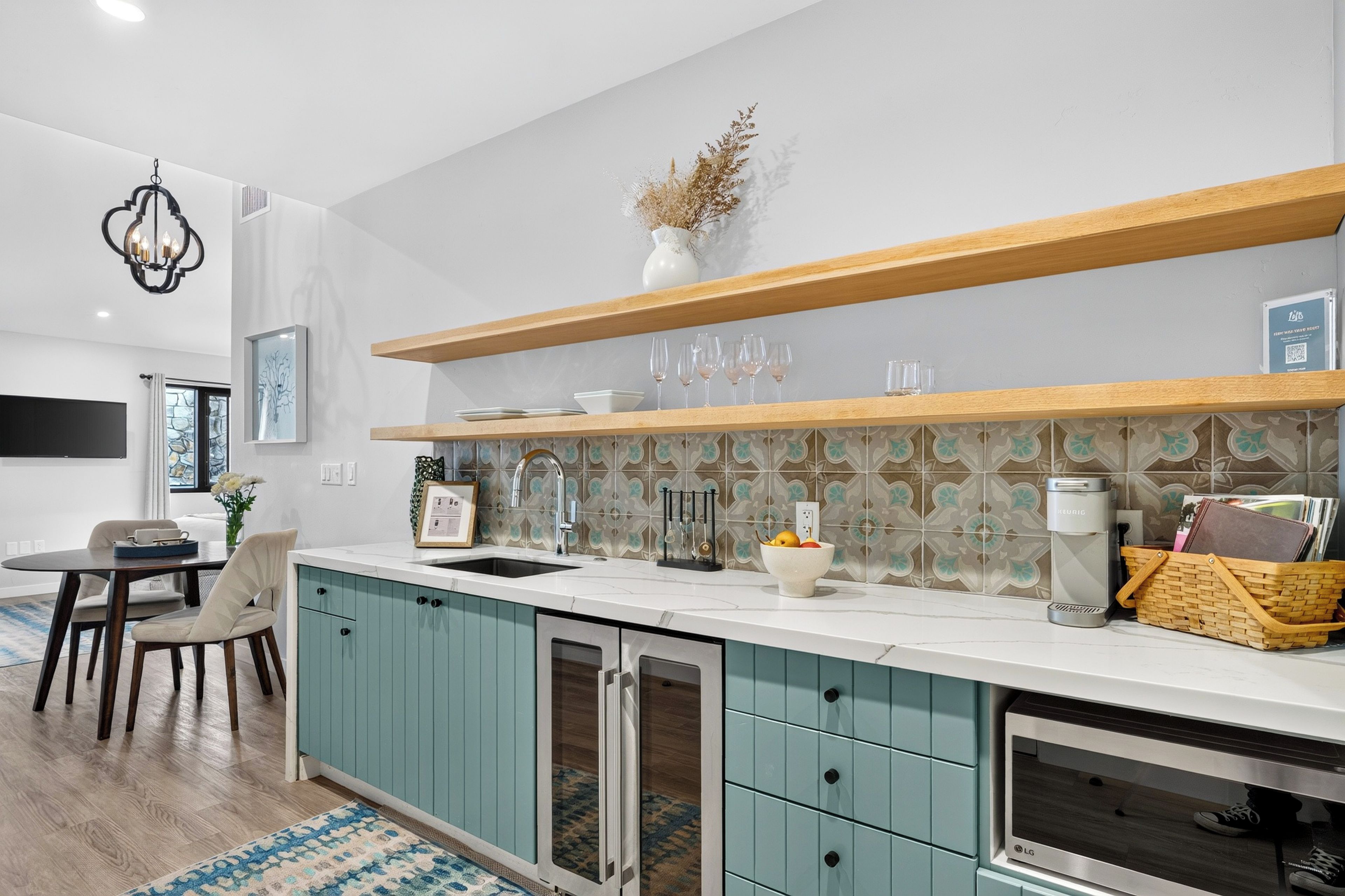 A modern kitchen with teal cabinets, a white countertop, and a backsplash with patterned tiles.