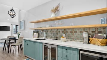 A modern kitchen with teal cabinets, a white countertop, and a backsplash with patterned tiles.