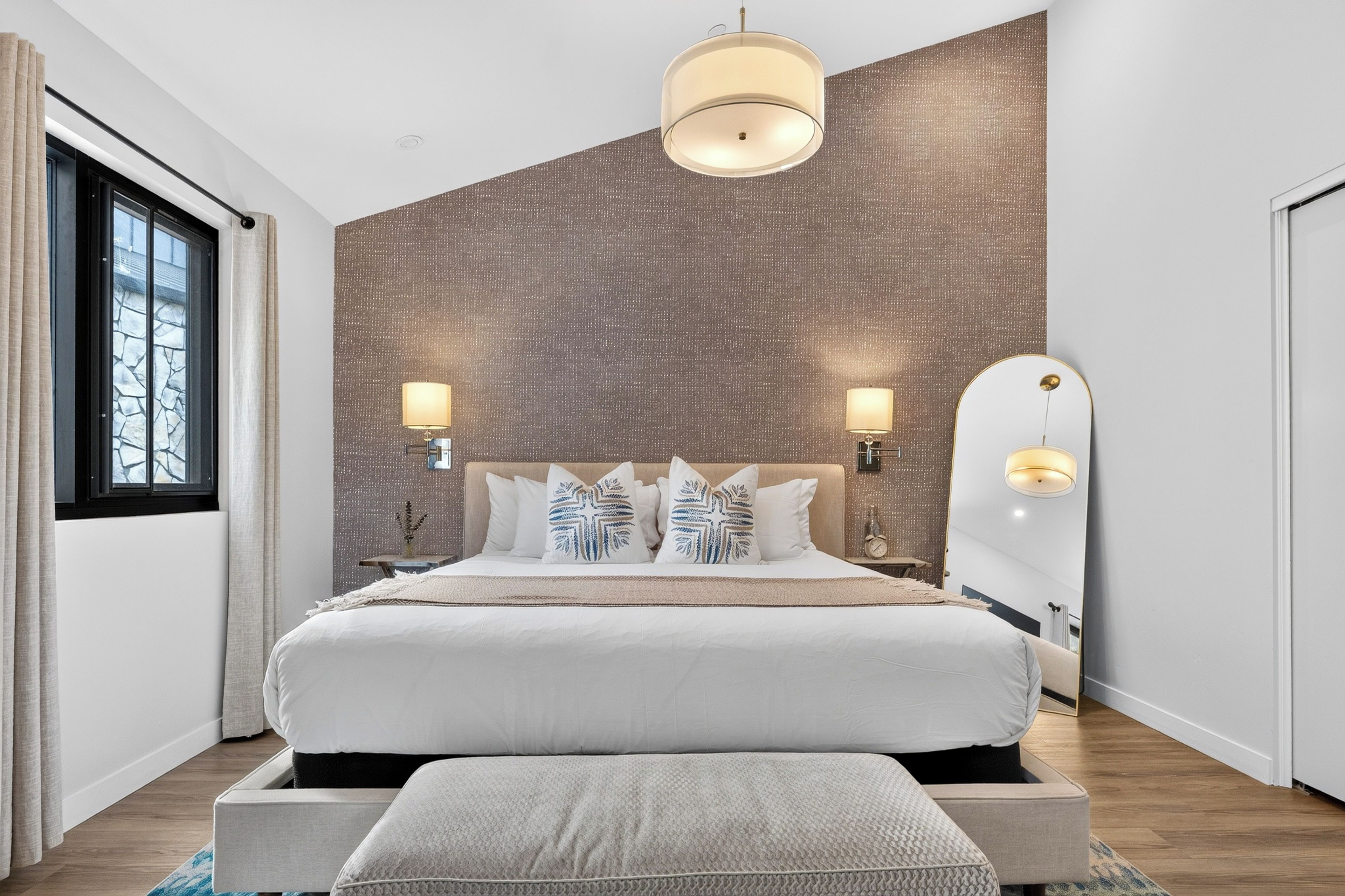Rest easy in the studio's king bed, framed by a textured accent wall, warm lighting, and a full-length mirror.