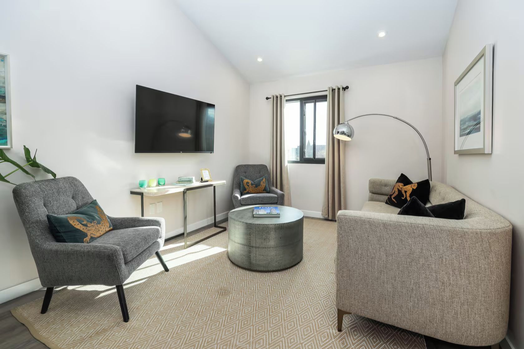 Una sala de estar moderna con un televisor de pantalla plana, dos sillones, una mesa de centro y un escritorio con una lámpara.