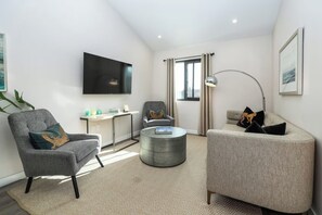 Una sala de estar moderna con un televisor de pantalla plana, dos sillones, una mesa de centro y un escritorio con una lámpara.