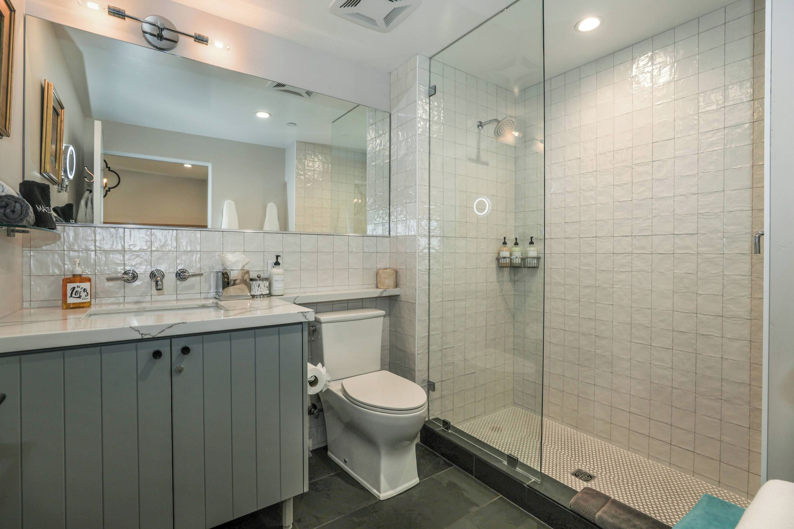 Un baño moderno con cabina de ducha de vidrio, inodoro blanco y tocador con espejo y perchero.