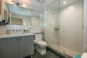 Un baño moderno con cabina de ducha de vidrio, inodoro blanco y tocador con espejo y perchero.