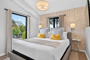 A modern hotel room with a large bed, two bedside lamps, a view of trees, and a patterned wallpaper. - Paso Market Walk + Wine Country | Near Downtown & Event Center | The Oak Room (Paso Robles)