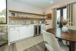 A modern kitchen with white cabinets, a built-in oven, and a dining area with a round table and chairs. - Paso Market Walk + Wine Country | Near Downtown & Event Center | The Oak Room (Paso Robles)