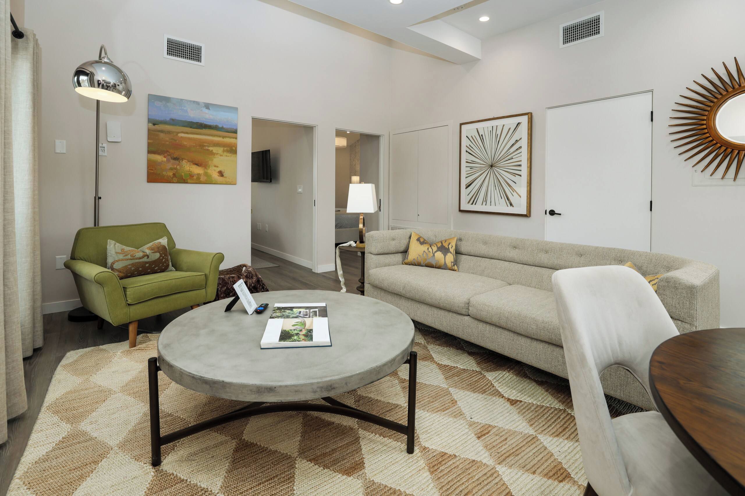 A living room with a green armchair, a grey sofa, a round coffee table, and a patterned rug.