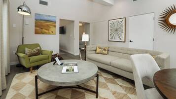 A living room with a green armchair, a grey sofa, a round coffee table, and a patterned rug.