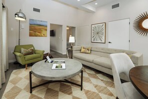 A living room with a green armchair, a grey sofa, a round coffee table, and a patterned rug. - Paso Market Walk + Wine Country | Near Downtown & Event Center | The Oak Room (Paso Robles)