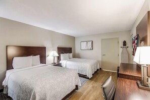 Una habitación de hotel con dos camas, un escritorio, una silla, una lámpara y una puerta.