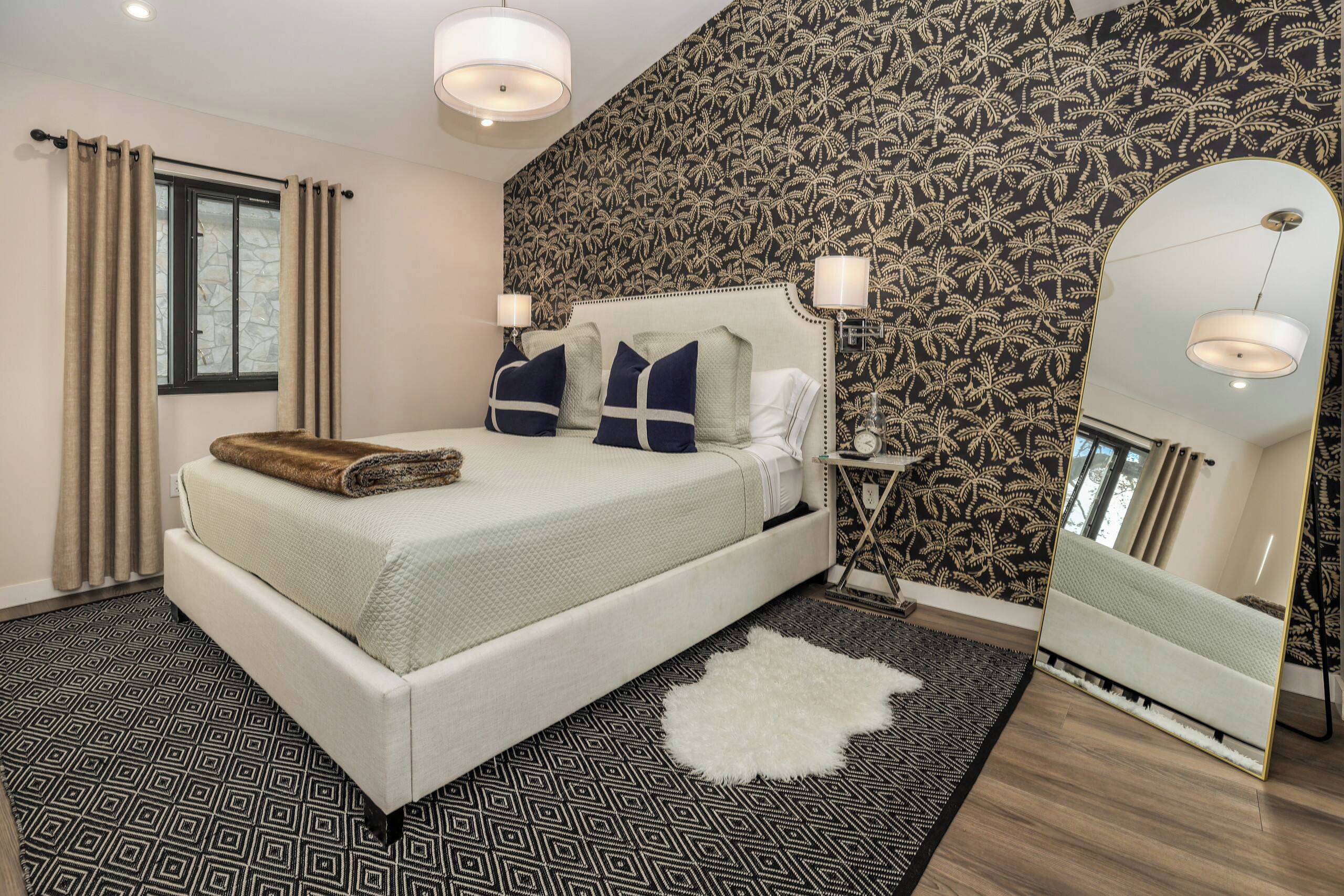 Un dormitorio con una cama, una mesita de noche, un espejo y una pared con diseño.
