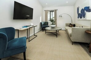 A modern living room with a flat-screen TV, a round coffee table, a sofa, and a blue armchair. - Paso Market Walk Studio • Walk To Downtown + Tasting Rooms | The Fig (Paso Robles)