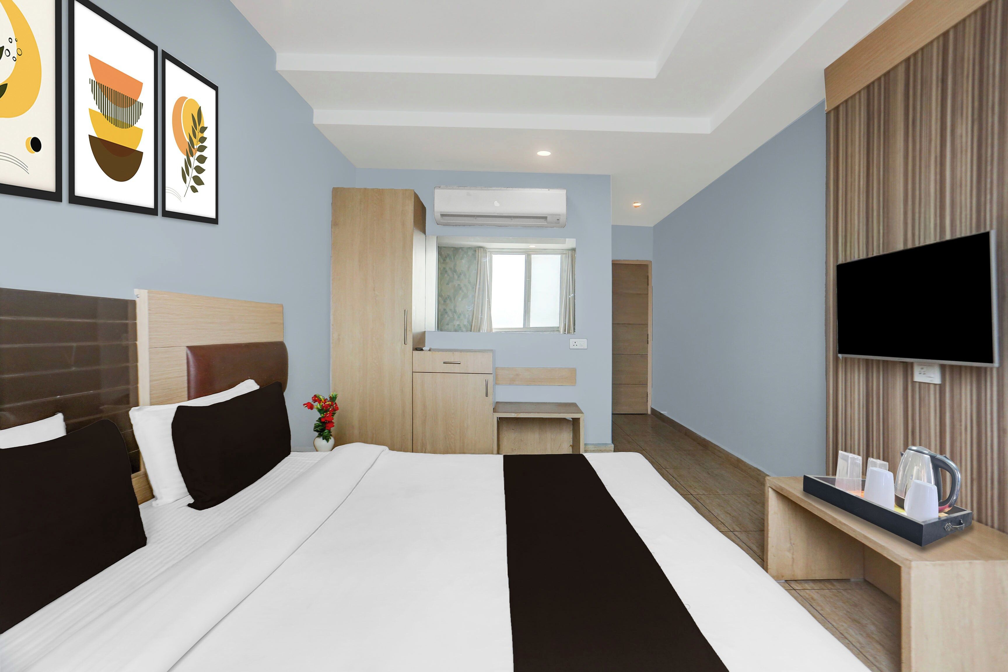 Habitación de hotel con cama, televisión, escritorio con hervidor y baño visible a través de una puerta abierta.