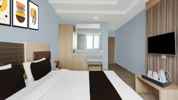 Habitación de hotel con cama, televisión, escritorio con hervidor y baño visible a través de una puerta abierta.