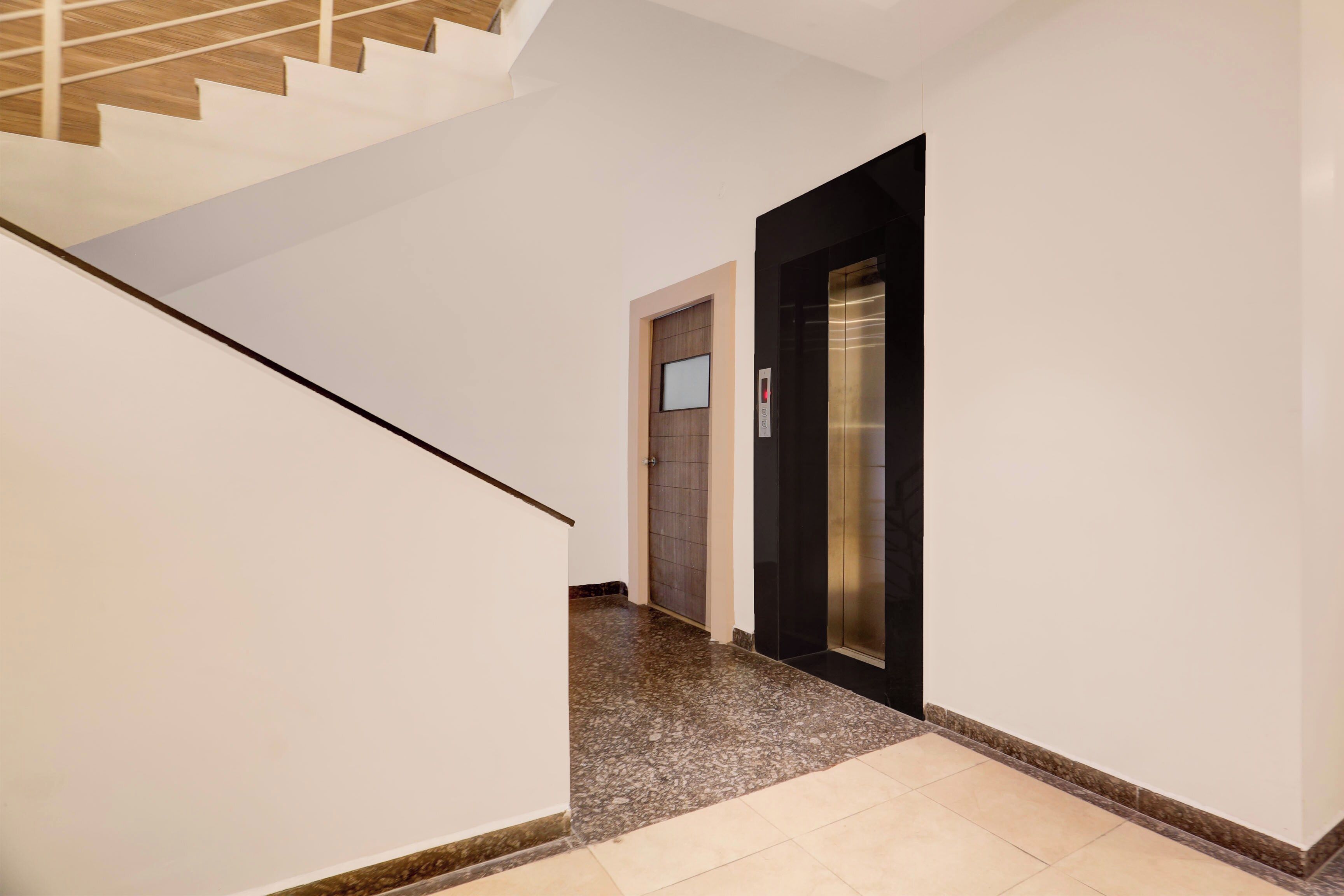 A hallway with a staircase on the left, a door with a window, and an elevator on the right.