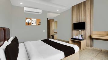 Habitación de hotel con cama, televisor, escritorio con tetera y aire acondicionado de pared.