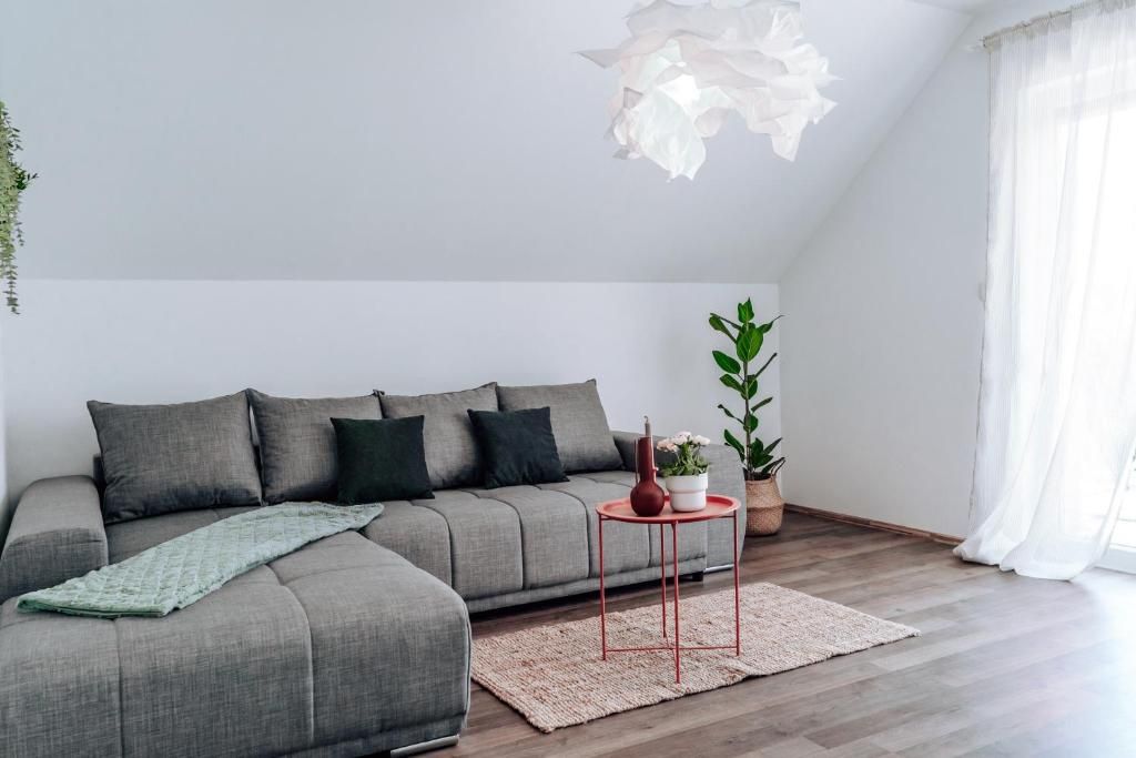 A modern living room with a grey sofa, a red side table, a potted plant, and a hanging light fixture.