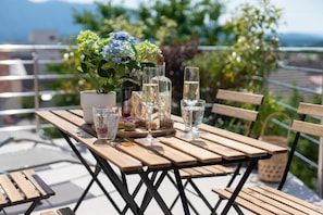 Ein Holztisch mit einer Topfpflanze, Gläsern und Flaschen auf einer Terrasse mit Blick.