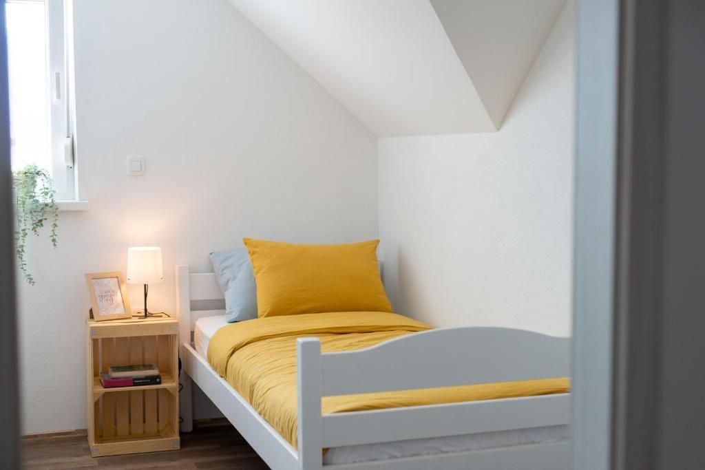 A small, single-bed room with a white headboard, a bedside table with a lamp, and a framed picture.