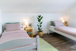 Quarto com duas camas de solteiro, mesas de cabeceira com luminárias, um vaso de planta e um tapete verde.