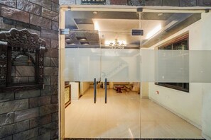 Vista interior de un vestíbulo de hotel con una recepción, una araña y una pared de piedra con un cartel.