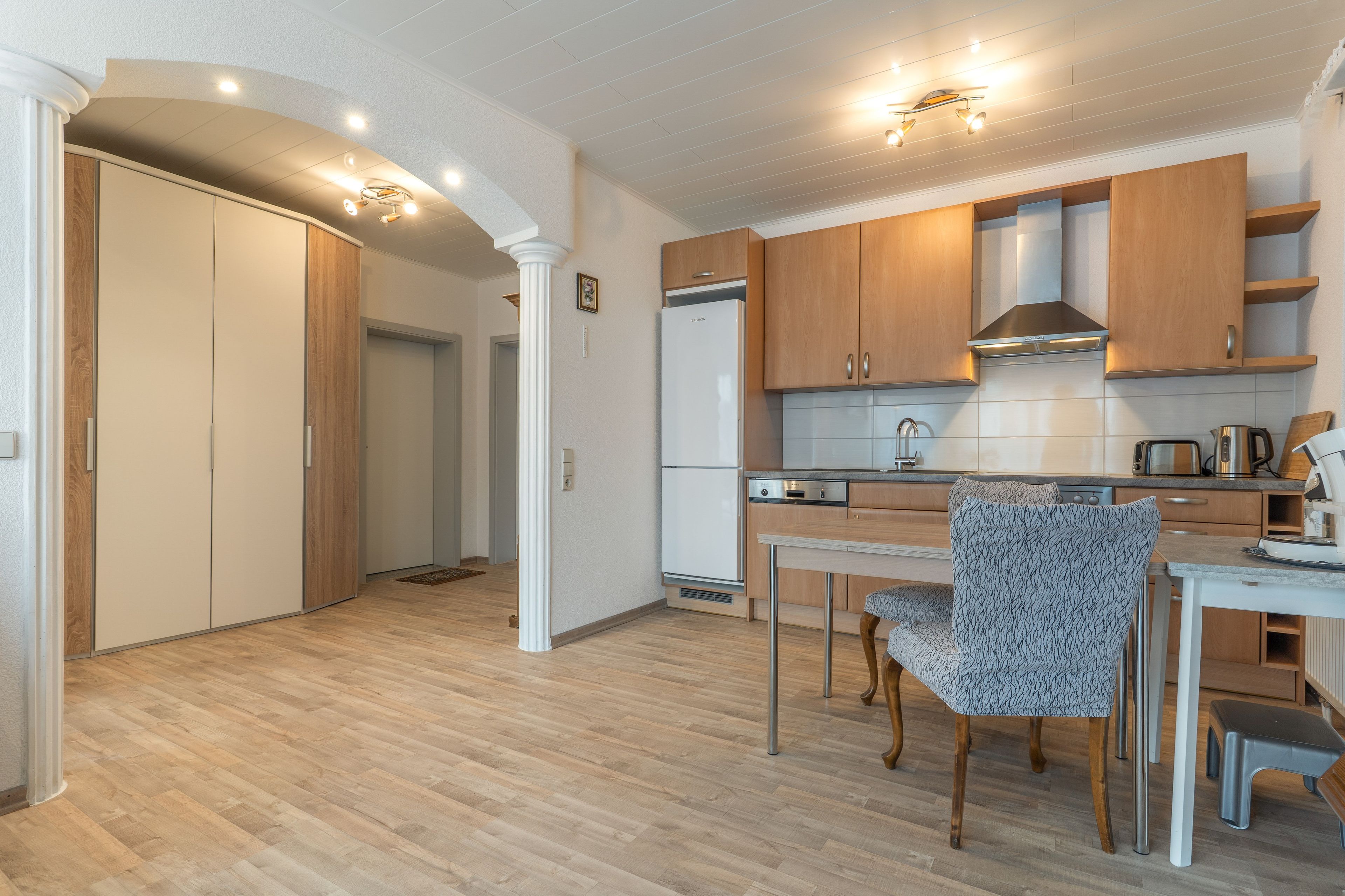 Une cuisine moderne avec des meubles en bois, une hotte en acier inoxydable et un coin repas agrémenté de chaises à motifs.