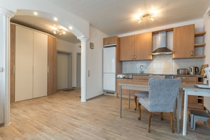 Eine moderne Küche mit Holzschränken, einer Edelstahl-Dunstabzugshaube und einem Essbereich mit einem gemusterten Stuhl.