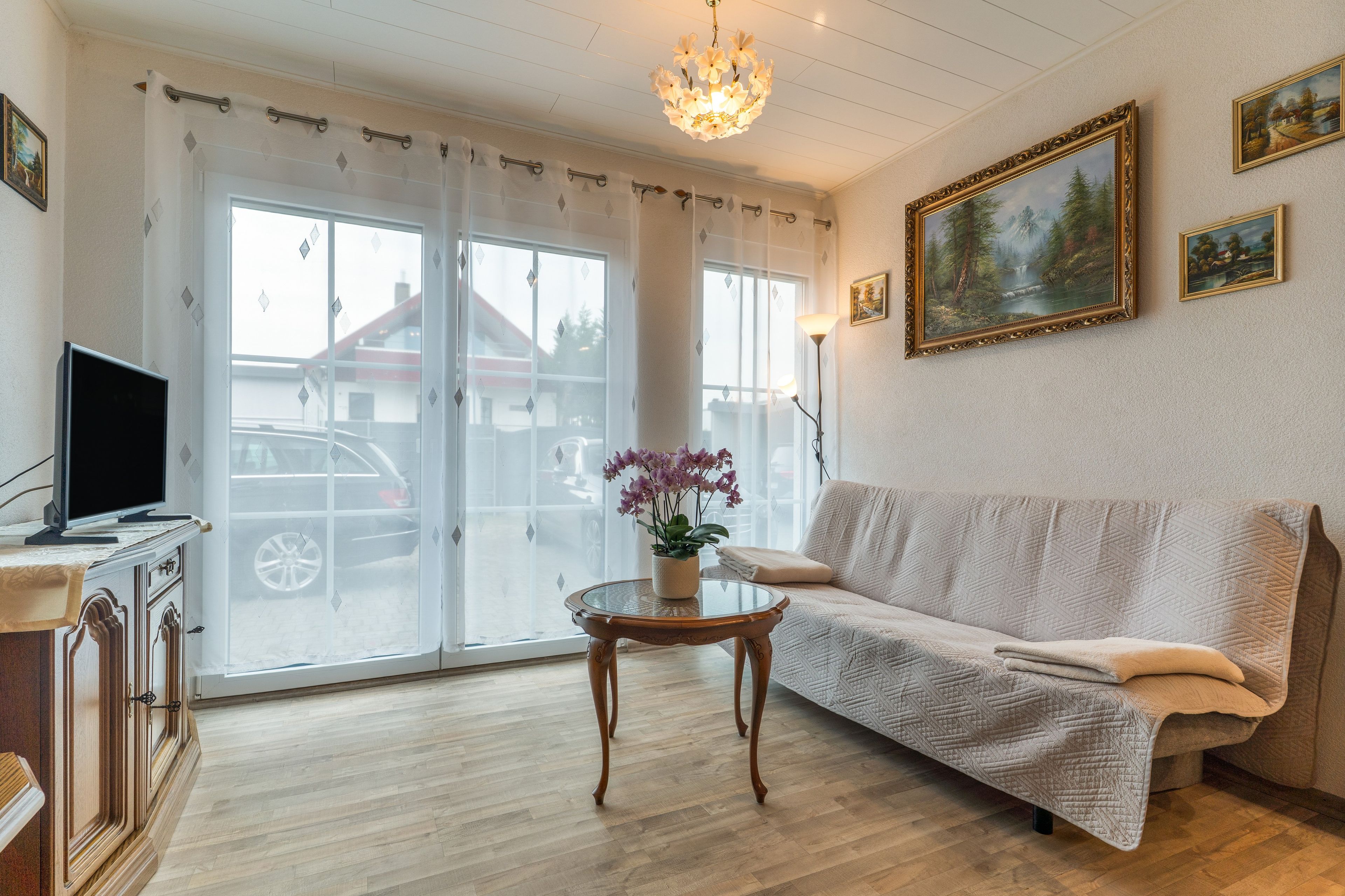 Ein Wohnzimmer mit einer Couch, einem Glastisch, einem Fernseher auf einem Schrank und einer Chandelier.
