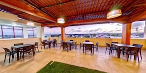 Un espacio de comedor al aire libre con varias mesas y sillas, techo de madera y vistas a la ciudad.