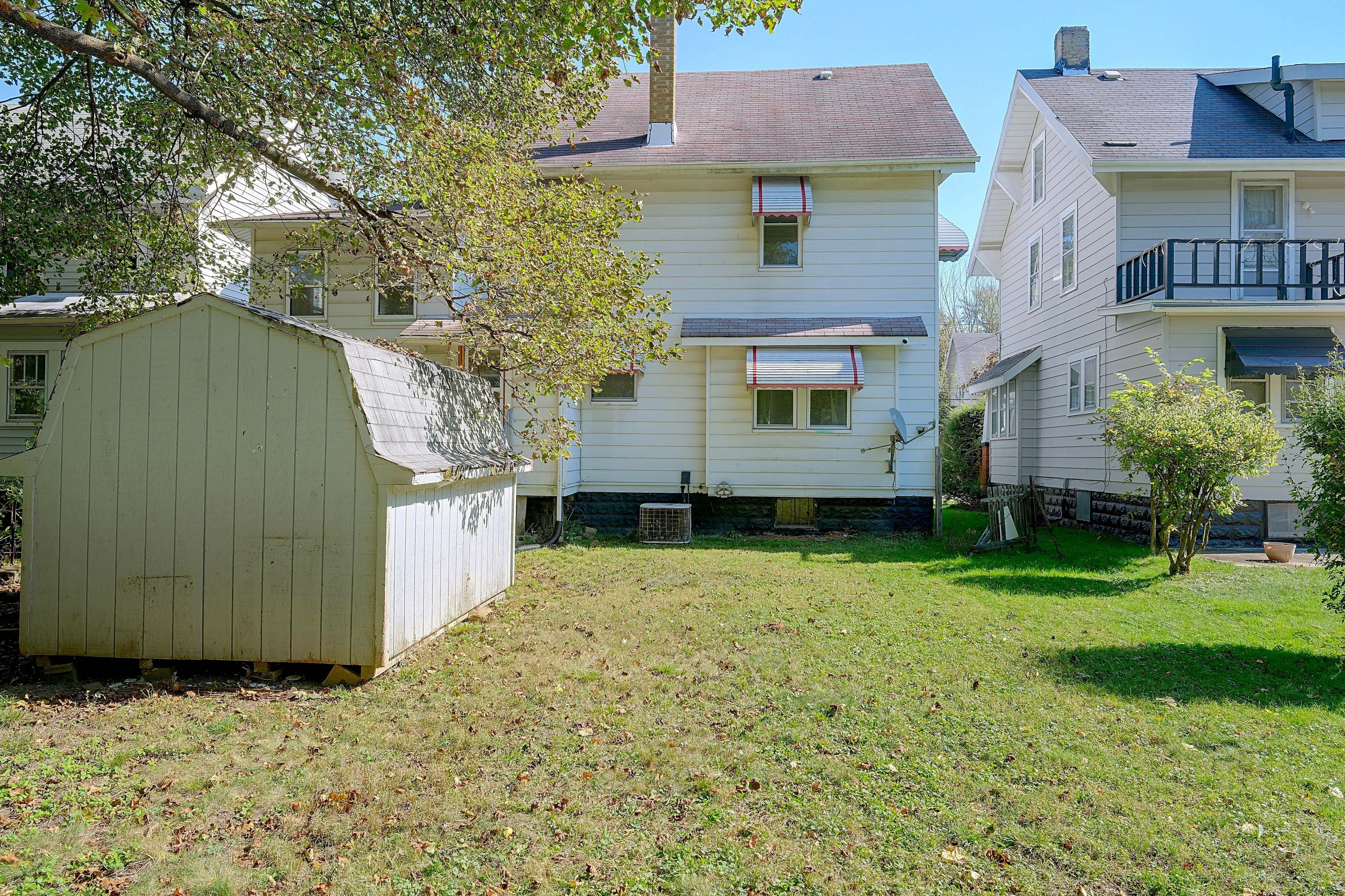 A residential area with a two-story house, a small shed, and a grassy yard.