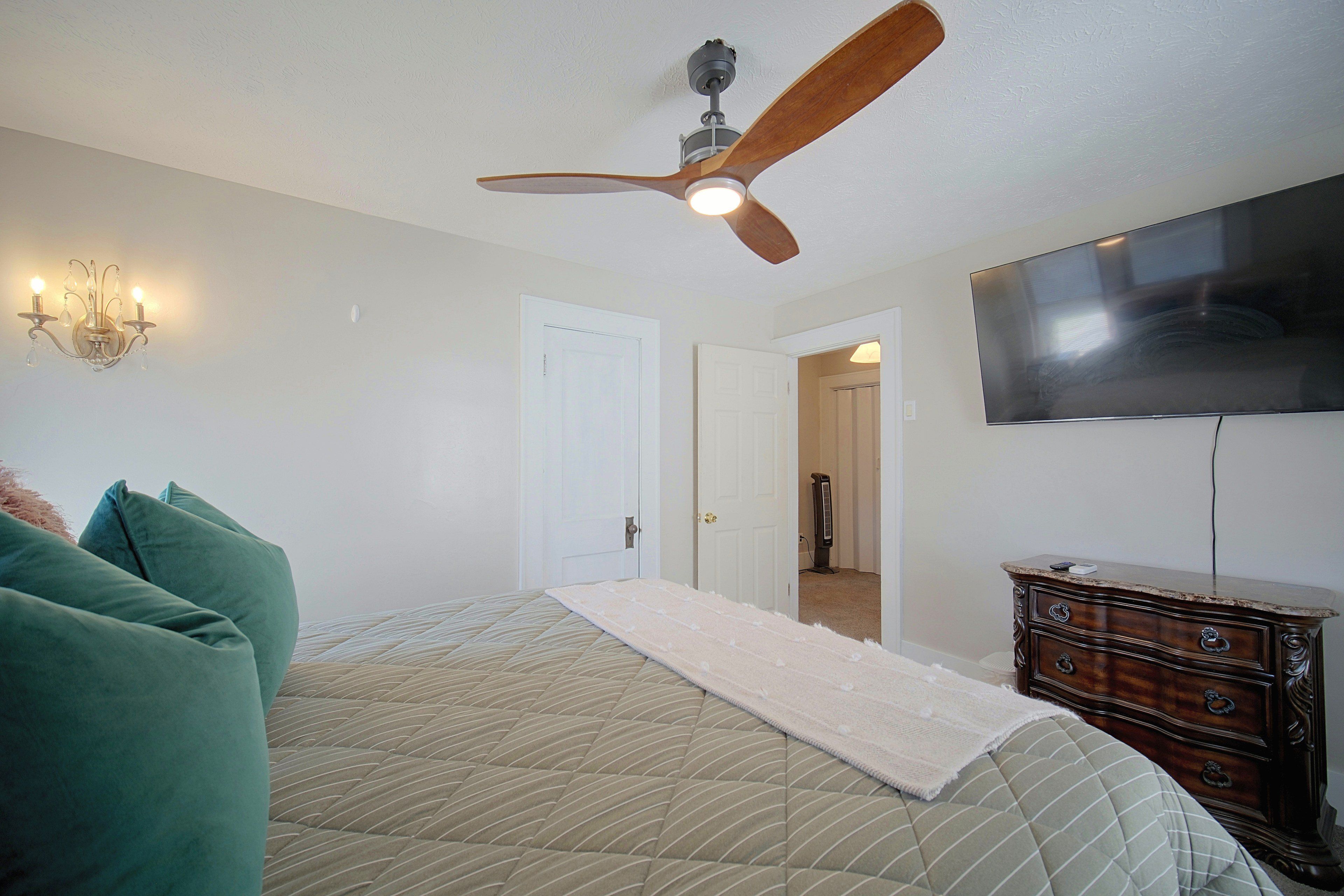 Une chambre à coucher avec un lit, un ventilateur de plafond, une commode et un téléviseur fixé au mur.