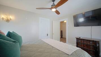 Une chambre à coucher avec un lit, un ventilateur de plafond, une commode et un téléviseur fixé au mur.