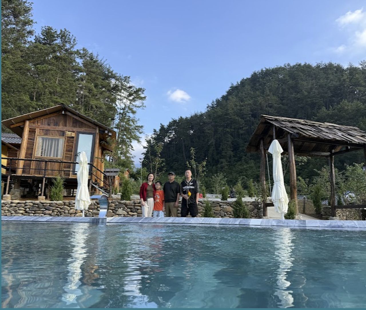 A pool area with a wooden deck, a stone wall, and a mountain backdrop.