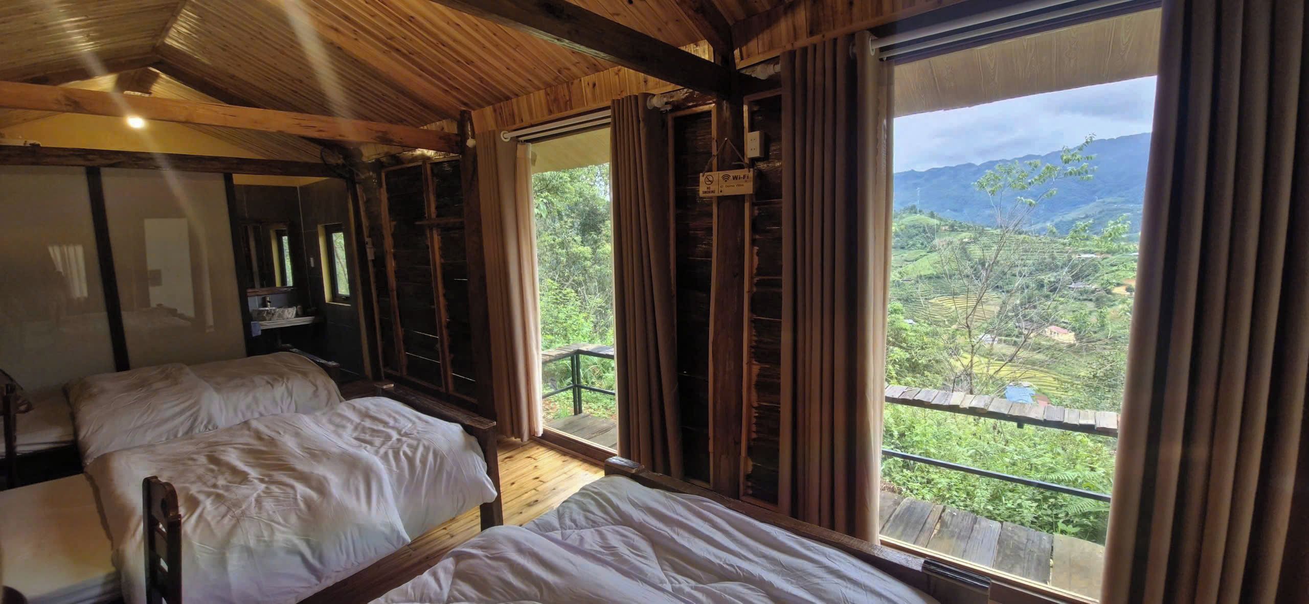 A room with two beds, a wooden ceiling, a window with a view of a mountainous landscape, and a sign indicating Wi-Fi availability.