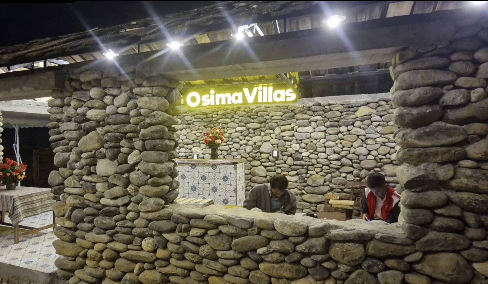 A stone-walled structure with a sign reading 'Osima Villas' and a tiled counter area.