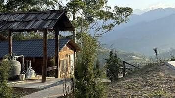 Una cabaña rústica con techo de metal, rodeada de árboles y una vista a montañas distantes.