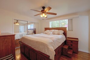 Quarto com cama de madeira, mesa de cabeceira, espelho e ventoinha no teto.