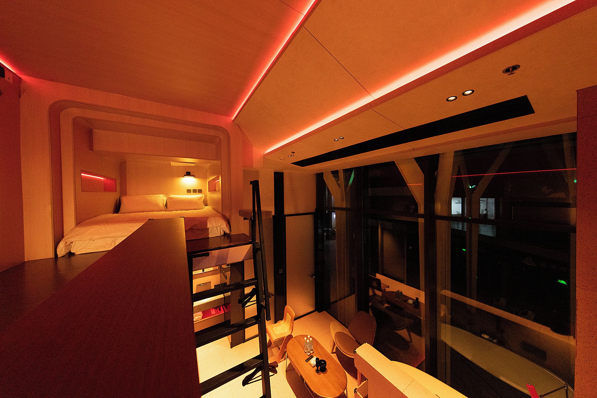 A modern hotel room with a bed, a desk, and a view of the city at night.