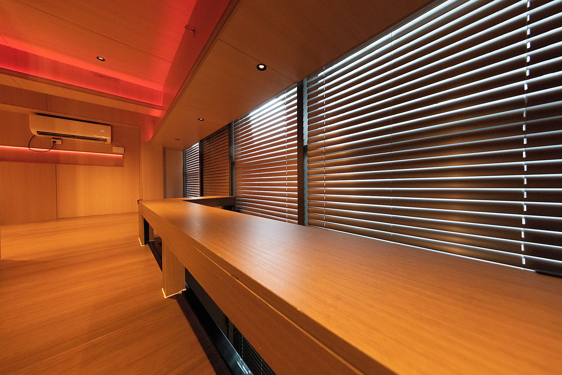 A modern interior with a wooden reception desk, horizontal blinds, and recessed ceiling lighting.