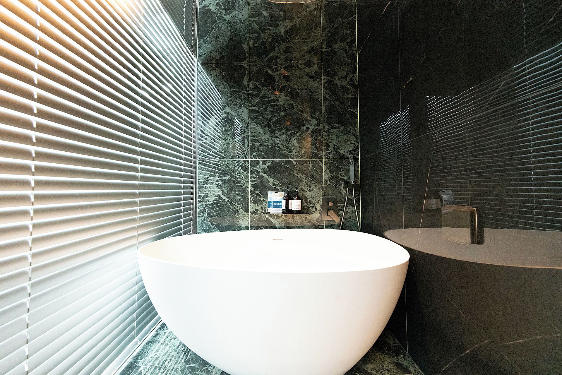 Un baño moderno con un lavabo grande de color blanco, paredes de mármol oscuro y una zona de ducha.