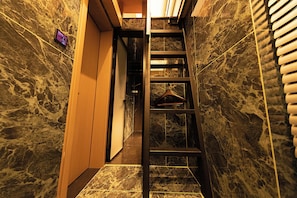 A narrow hallway with a wooden door on the left and a staircase leading to a landing. - X Hotel (Tongzhou)