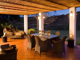 Un patio exterior con mesa y sillas, rodeado por una pérgola e iluminación decorativa.