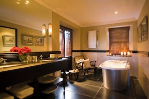 Une salle de bain moderne dotée d’un grand miroir, de deux vasques, d’une baignoire et d’un coin salon avec une chaise et une table.