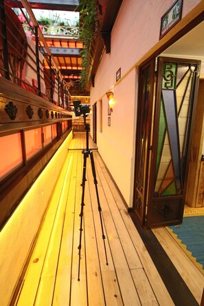 Un pasillo con piso de madera, un trípode de cámara y una puerta con un diseño geométrico de vidrio.